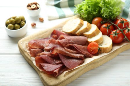 Photo for Board with delicious bresaola served with bread and tomato on white wooden table - Royalty Free Image