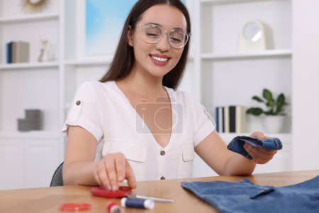 Happy woman holding cut hem and jeans at table indoors