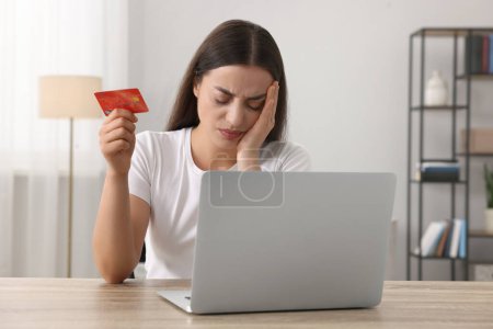 Photo for Stressed woman with credit card and laptop at table indoors. Be careful - fraud - Royalty Free Image
