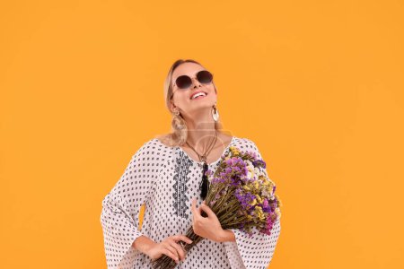 Porträt einer lächelnden Hippie-Frau mit Blumenstrauß auf gelbem Hintergrund