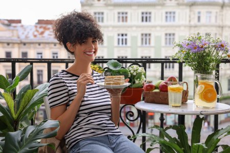 Téléchargez les photos : Jeune femme manger morceau de gâteau sur le balcon avec de belles plantes d'intérieur - en image libre de droit