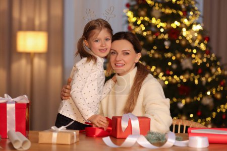 Envoltura de regalos de Navidad. Madre y su hija pequeña en la mesa con cajas de regalo, decoración en la habitación