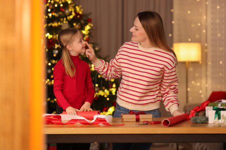 Envoltura de regalos de Navidad. Madre y su hija pequeña decorando cajas de regalo en casa