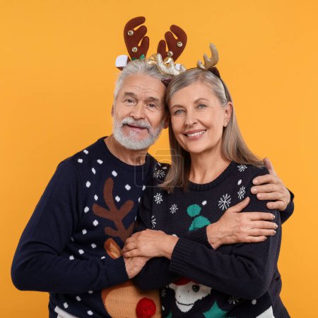 Seniorenpaar in Weihnachtspullis und Rentier-Stirnbändern auf orangefarbenem Hintergrund