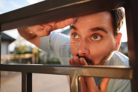 Konzept des Privatlebens. Neugieriger Mann spioniert Nachbarn über Zaun im Freien aus