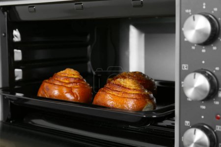 Open electric oven with delicious pastry, closeup
