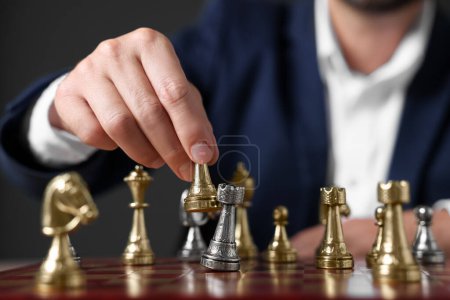 Man with game piece playing chess at checkerboard against dark background, closeup