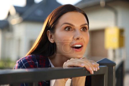 Foto de Concepto de vida privada. Mujer joven curiosa espiando a los vecinos sobre la valla al aire libre - Imagen libre de derechos