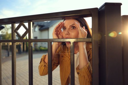 Téléchargez les photos : Concept de vie privée. Femme curieuse espionnant les voisins au-dessus de la clôture à l'extérieur - en image libre de droit