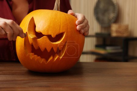 Frau schnitzt Kürbis für Halloween an Holztisch drinnen, Nahaufnahme