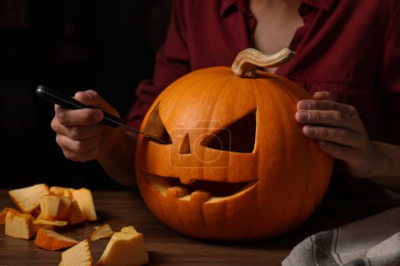 Frau schnitzt Kürbis für Halloween an Holztisch, Nahaufnahme