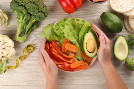 Dieta saludable. Mujer con verduras frescas y cinta métrica en la mesa de madera ligera, vista superior