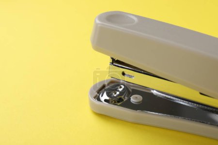Beige stapler on yellow background, closeup. Space for text