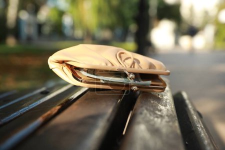 Monedero de cuero beige en banco de madera al aire libre, primer plano. Perdido y encontrado