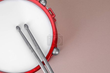 Drum and sticks on dusty rose background, top view with space for text. Percussion musical instrument