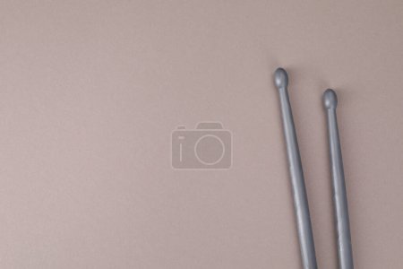 Two gray drum sticks on dusty rose background, top view. Space for text