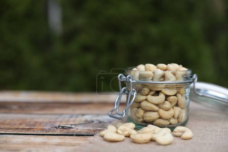 Tasty cashew nuts in glass jar on wooden table outdoors, space for text