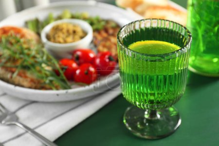 Délicieuse boisson avec estragon en verre sur table verte, gros plan. Espace pour le texte