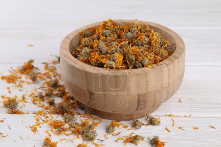 Bowl with dry calendula flowers on white wooden table, closeup