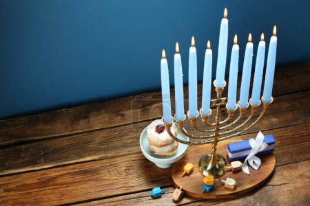 Chanukka-Feier. Menora mit brennenden Kerzen, Dreidels, Donuts und Geschenkschachtel auf Holztisch, oben Blick. Raum für Text