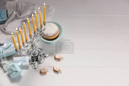 Foto de Celebración de Hanukkah. Menorah con velas encendidas, dreidels y cajas de regalo en mesa de madera blanca, por encima de la vista. Espacio para texto - Imagen libre de derechos