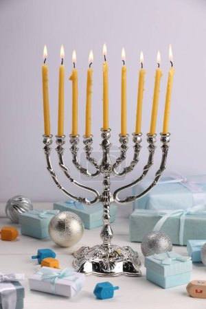 Téléchargez les photos : Hanoukka fête. Menorah avec des bougies allumées. dreidels, coffrets cadeaux et ornements de vacances sur table en bois blanc - en image libre de droit