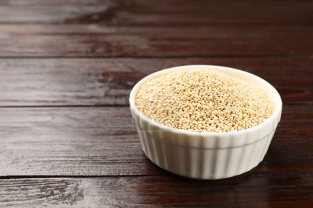 Dry quinoa seeds in bowl on wooden table, space for text