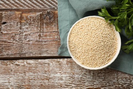 Photo for Dry quinoa seeds in bowl and parsley on wooden table, top view. Space for text - Royalty Free Image