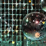 Shiny disco balls against foil party curtain under color lights, space for text. Bokeh effect