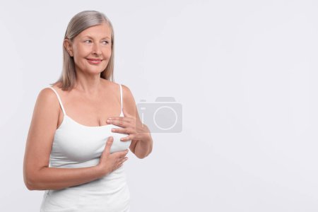 Beautiful senior woman doing breast self-examination on white background, space for text