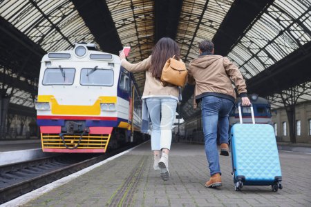 Photo for Being late. Couple with suitcase running towards train at station, back view. Space for text - Royalty Free Image