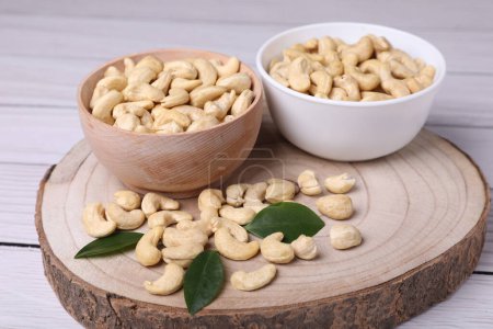 Tasty cashew nuts and green leaves on light wooden table