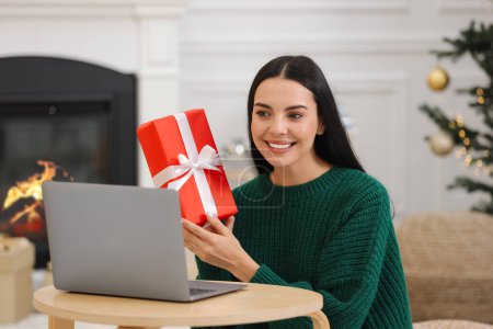 Celebrando la Navidad en línea con regalos intercambiados por correo. Mujer sonriente con caja de regalo durante la videollamada en el ordenador portátil en casa