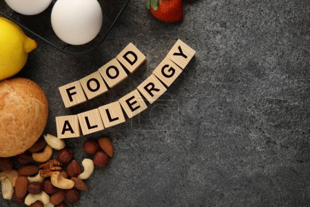 Alergia alimentaria. Diferentes productos frescos y cubos de madera sobre mesa gris, plano con espacio para el texto
