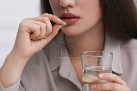 Woman with glass of water taking antidepressant pill on light grey background, closeup