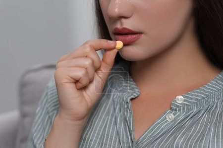 Woman taking antidepressant pill on light grey background, closeup