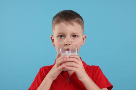 Téléchargez les photos : Mignon garçon boire du lait frais à partir de verre sur fond bleu clair - en image libre de droit
