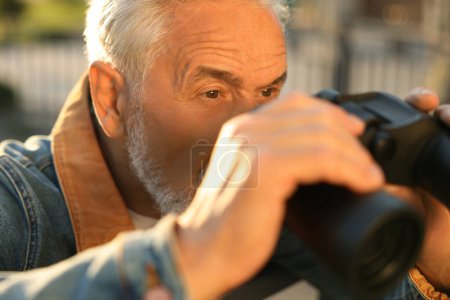 Téléchargez les photos : Concept de vie privée. Homme âgé curieux avec des jumelles espionnant les voisins à l'extérieur, gros plan - en image libre de droit
