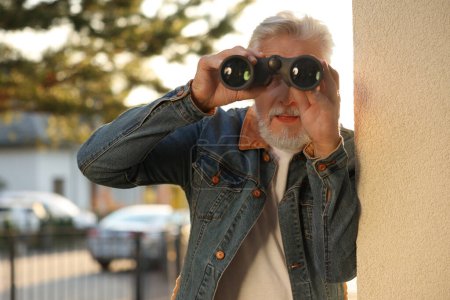 Téléchargez les photos : Concept de vie privée. Homme âgé curieux avec des jumelles espionnant les voisins à l'extérieur - en image libre de droit