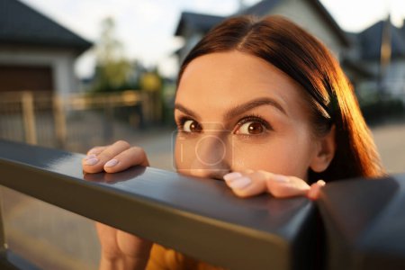 Konzept des Privatlebens. Neugierige junge Frau spioniert Nachbarn über Zaun im Freien aus