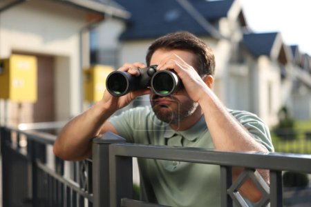Téléchargez les photos : Concept de vie privée. Homme curieux avec des jumelles espionnant les voisins au-dessus de la clôture à l'extérieur - en image libre de droit