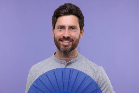 Happy man holding hand fan on purple background