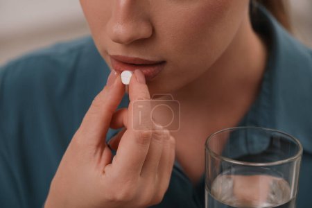 Woman with glass of water taking antidepressant pill, closeup