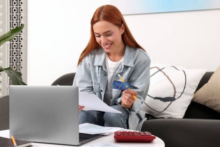 Téléchargez les photos : Femme avec carte de crédit utilisant un ordinateur portable pour payer les taxes en ligne à la maison - en image libre de droit
