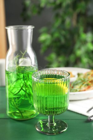 Délicieuse boisson avec estragon en verre sur table verte. Espace pour le texte