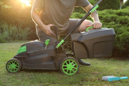 Cleaning lawn mower. Man detaching grass catcher from device in garden, closeup