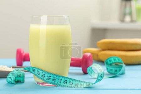 Tasty shake and measuring tape on light blue wooden table, closeup. Weight loss