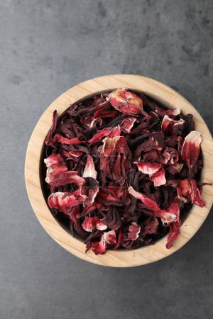 Hibiscus tea. Wooden bowl with dried roselle calyces on grey table, top view