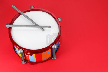 Colorful drum and sticks on red background, space for text. Percussion musical instrument