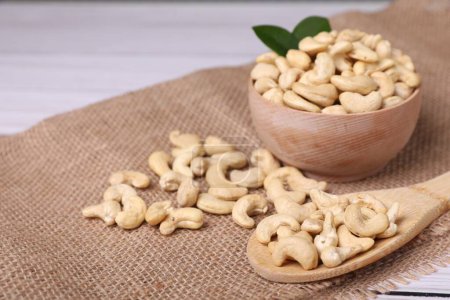 Tasty cashew nuts and green leaves on table, closeup. Space for text